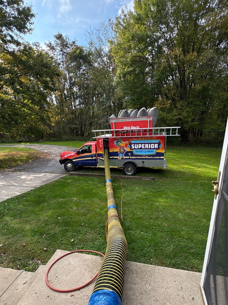 Yellow vacuum hose running across a front lawn from the house to the Superior truck parked in the driveway