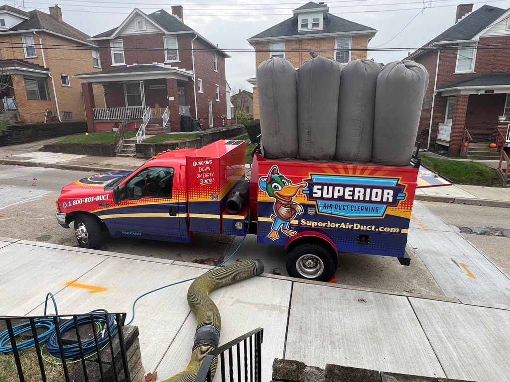 Superior duct-cleaning truck parked curbside on a residential street with the vacuum hose connected and running to the home
