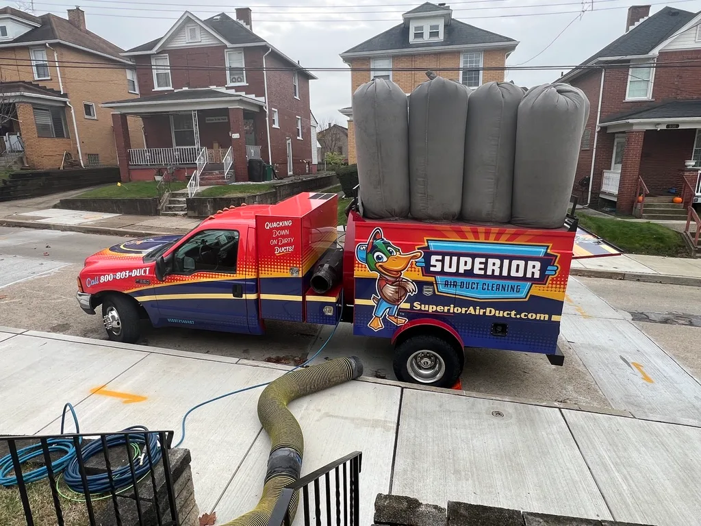 A Superior Air Duct Cleaning vacuum truck parked at the curb with the negative-pressure hose running into a customer's home