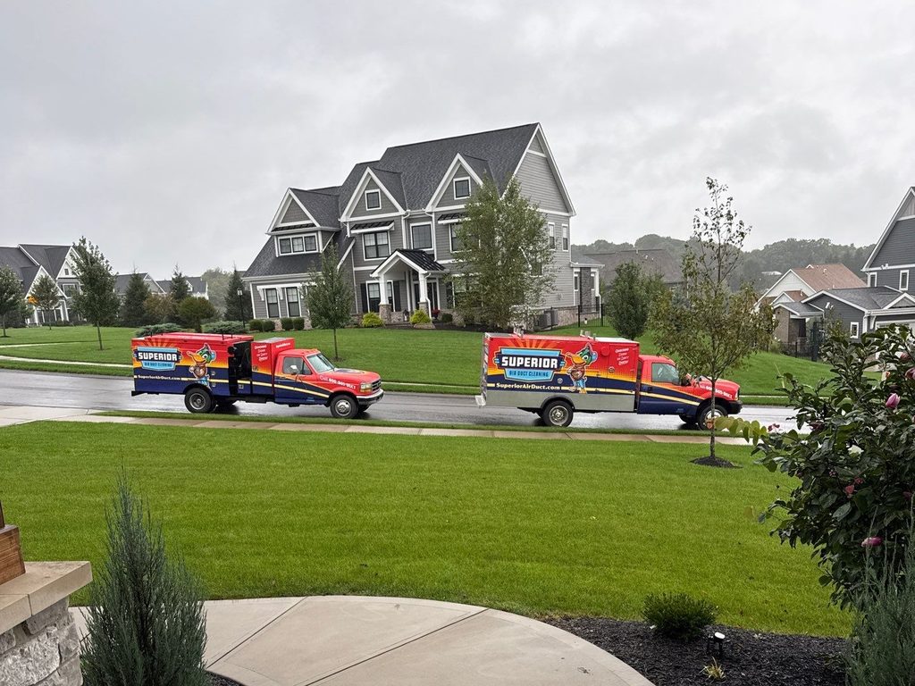 Two Superior Air Duct Cleaning trucks parked at the curb in front of a large two-story home on a residential job