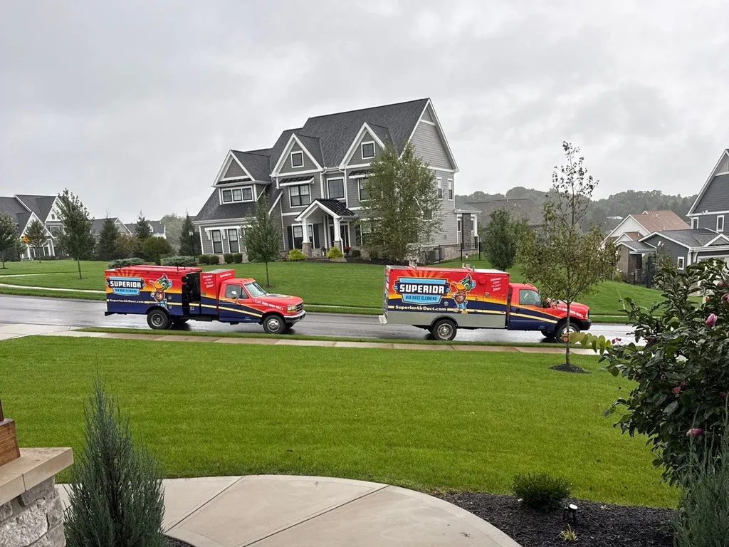 Two Superior Air Duct Cleaning trucks parked in front of a customer's home on a job