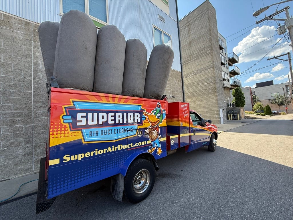 Superior Air Duct Cleaning box truck with gray negative-pressure filter bags loaded on top, parked in a brick alley on a sunny day
