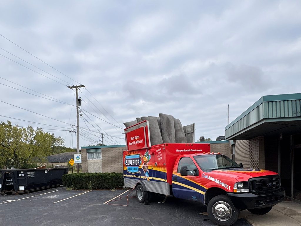Superior Air Duct Cleaning truck with gray filter bags loaded on top, parked beside a commercial building