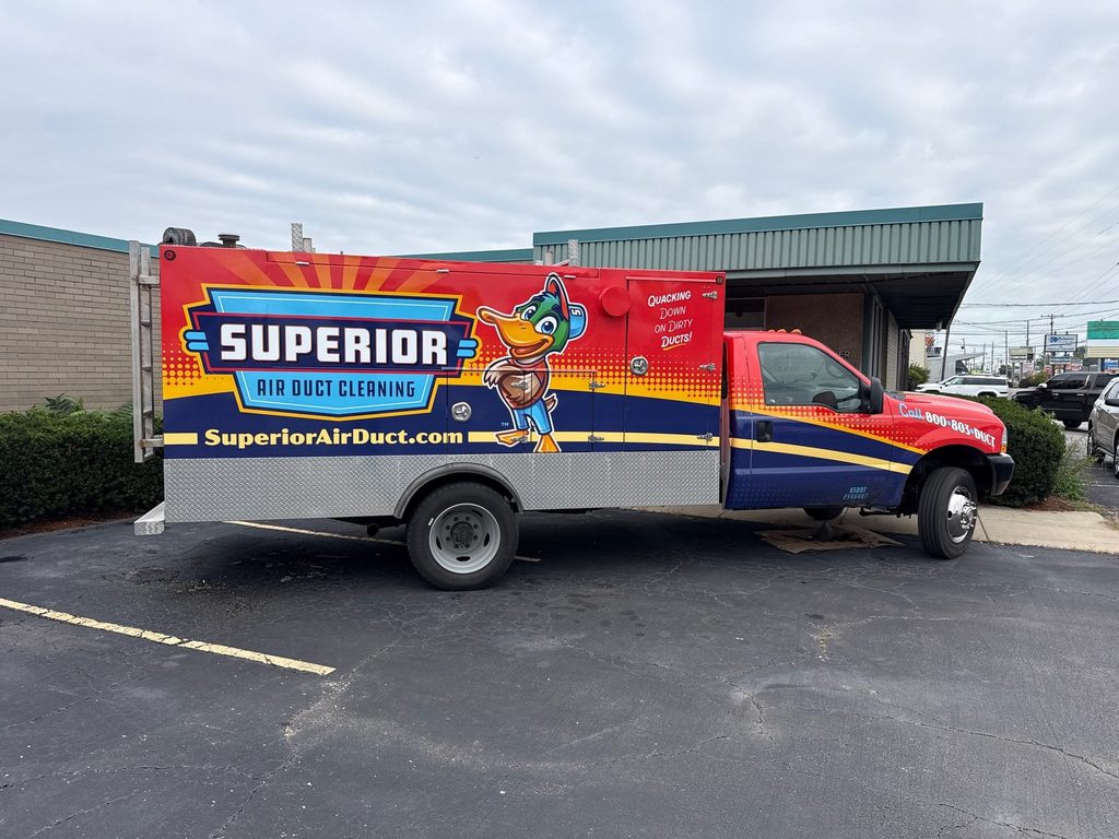 Side view of a Superior Air Duct Cleaning box truck with the duck mascot wrap, parked in a commercial parking lot