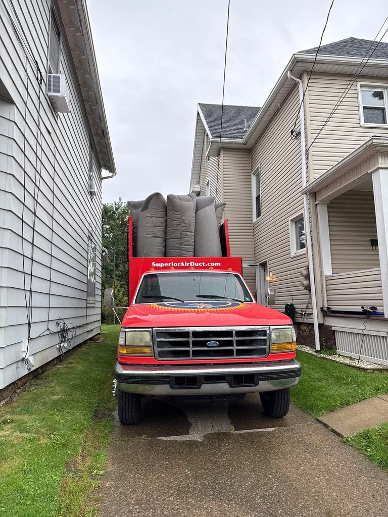 Front of a Superior Air Duct Cleaning truck with filter bags up, parked in a driveway between two houses