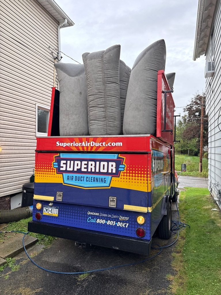 Rear of a Superior Air Duct Cleaning truck with filter bags loaded, parked in a driveway beside a house