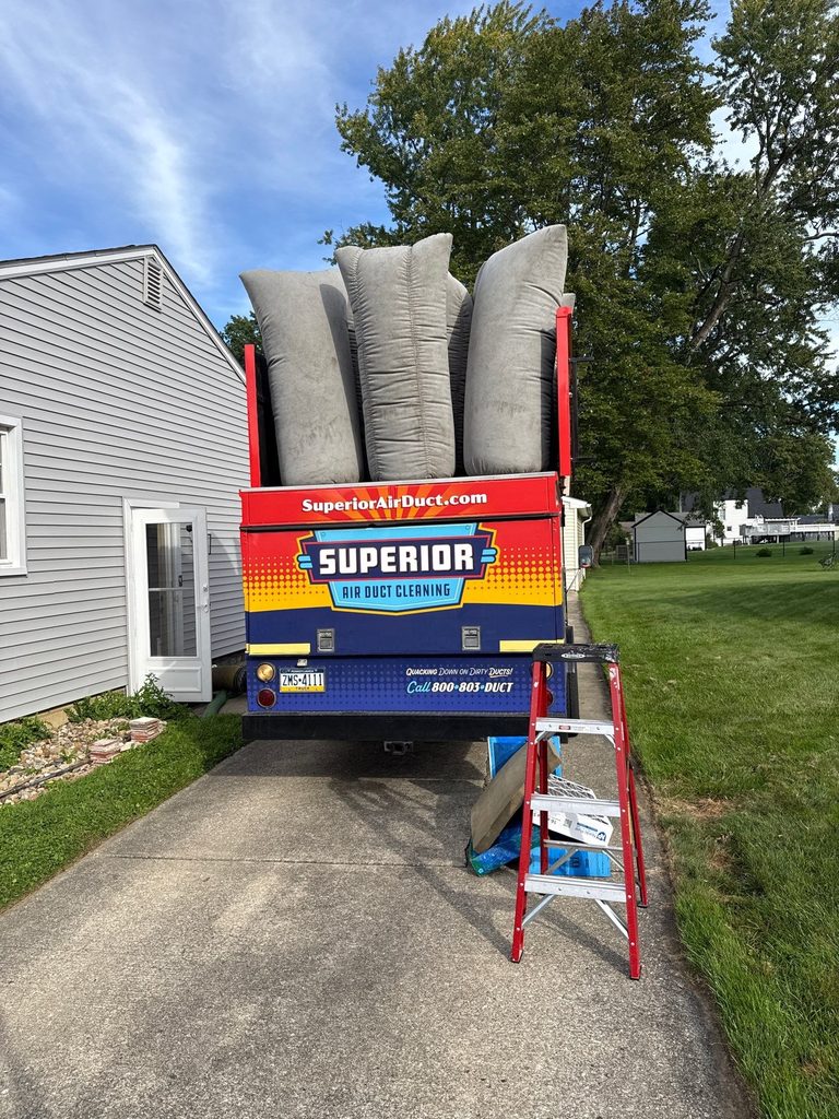 Rear of a Superior Air Duct Cleaning truck with filter bags up, parked in a driveway next to a house with a ladder beside it