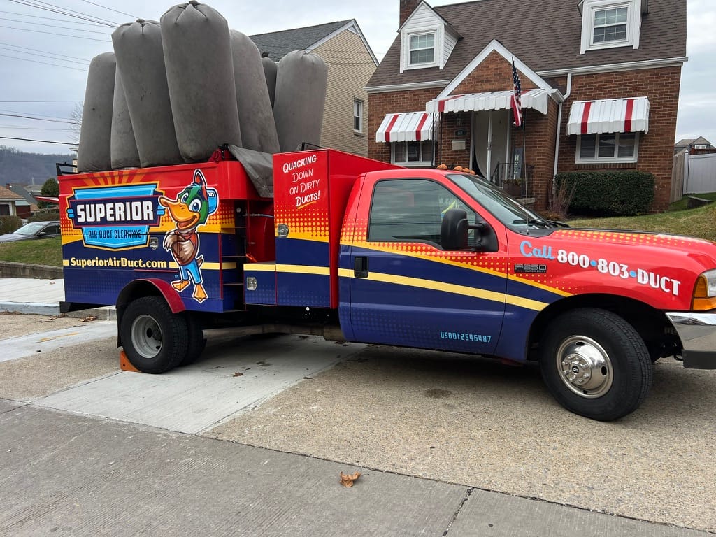 Superior duct-cleaning truck with filter bags loaded, parked outside a brick house with red-and-white awnings on a winter service call