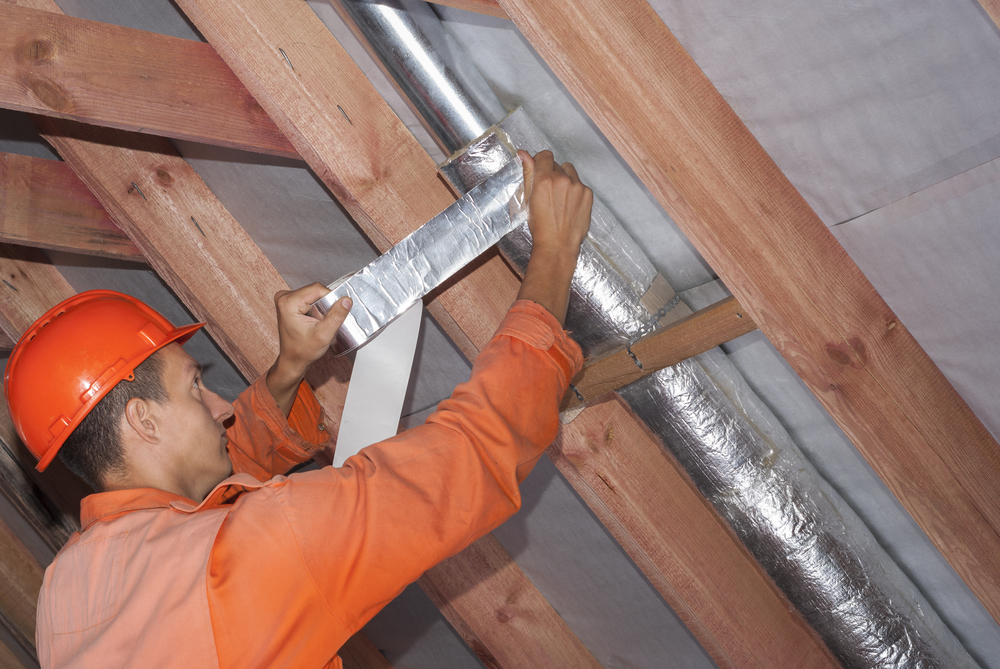 Man wrapping circular air duct in silver fiberglass insulation