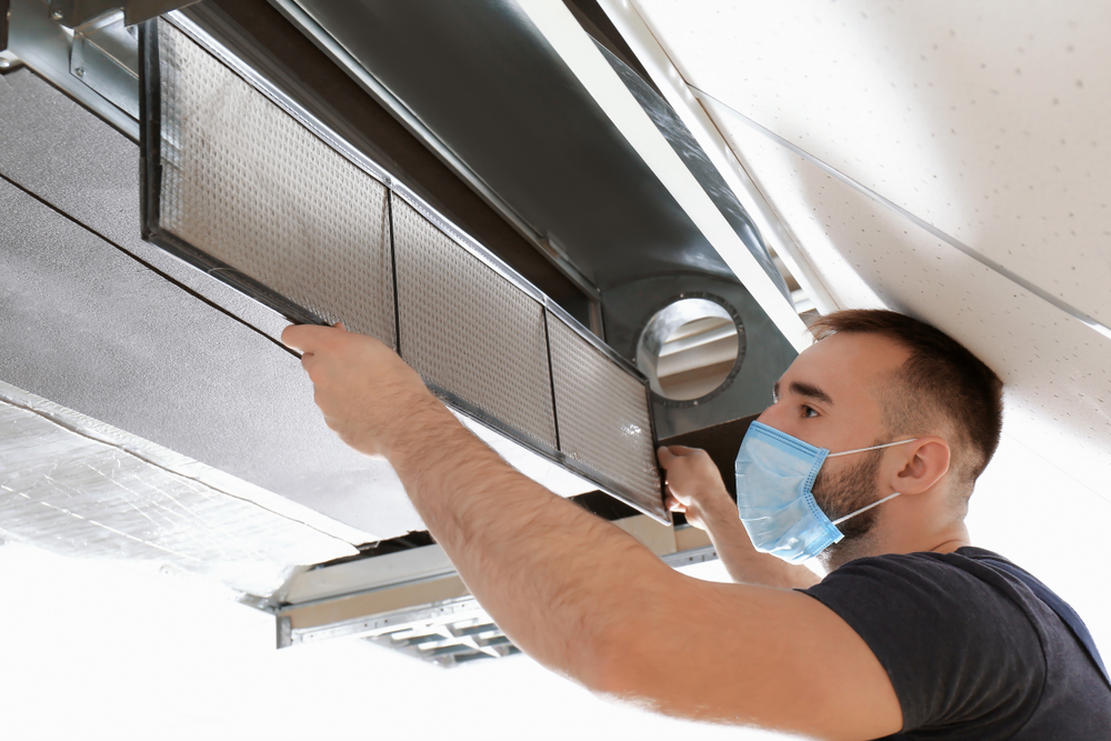 Man wearing a mask cleaning an air duct