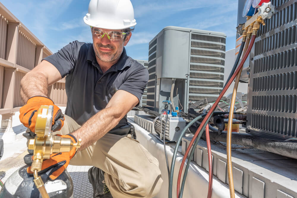 man in a white hardhat performing maintenance on an HVAC