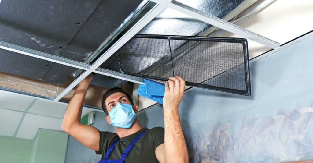 Masked air duct technician cleaning vent system